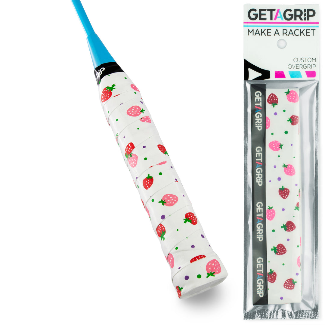 A custom overgrip for a badminton racket, featuring a white base with a strawberry and polka dot pattern, shown both applied to a racket handle and in its retail packaging by Get Grip.